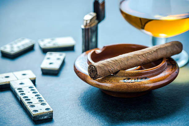 Cuban cigar in ashtray and domino game. On dark background.